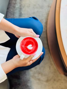 Close-up of a vibrant red coffee with heart-shaped foam art held in hands, Oman.