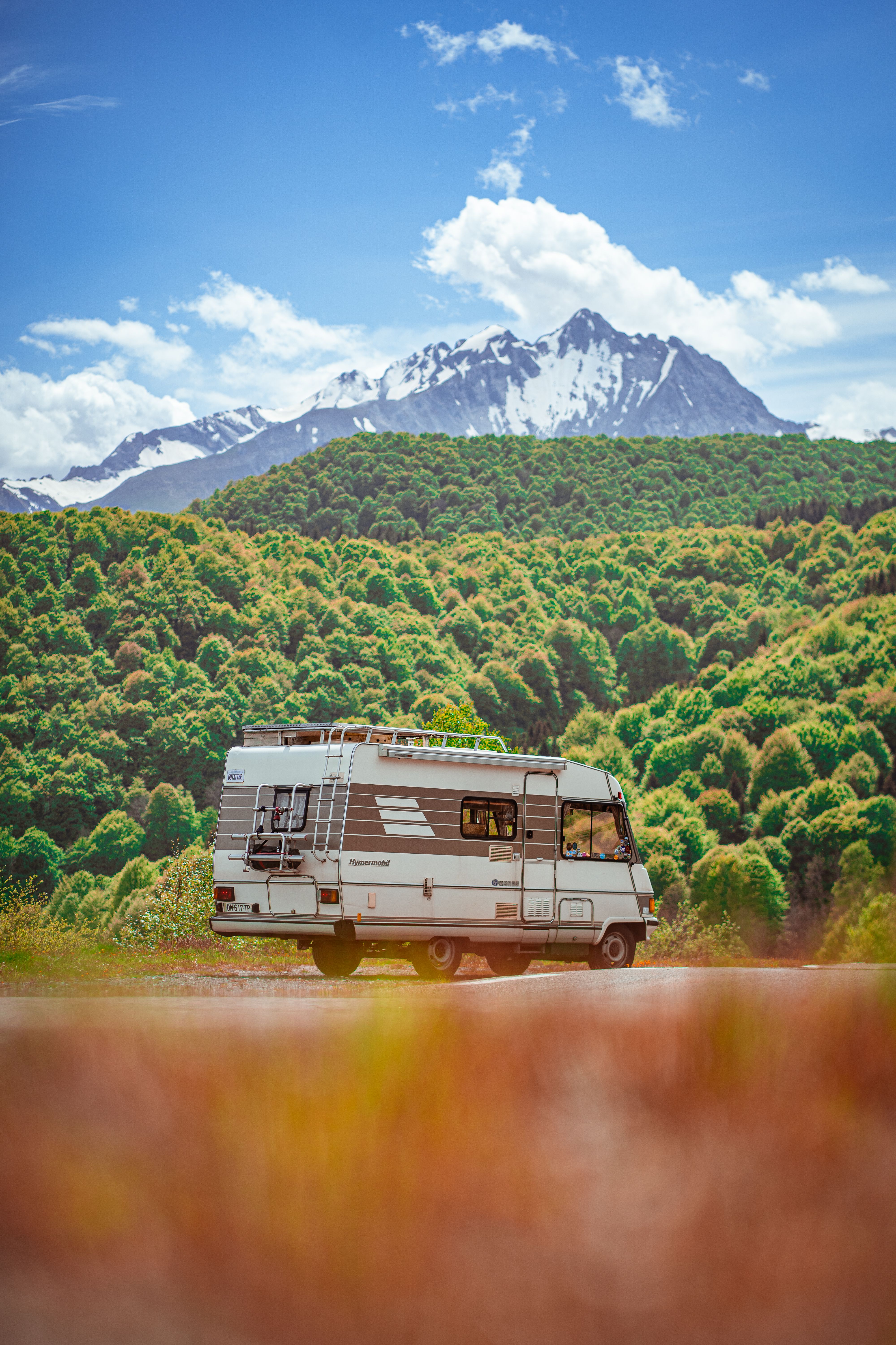 A classic camper van parked in front of a majestic snow-capped mountain range under a bright blue sky.