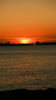 A tranquil ocean sunset with silhouetted ships on the horizon, creating a warm and peaceful scene.