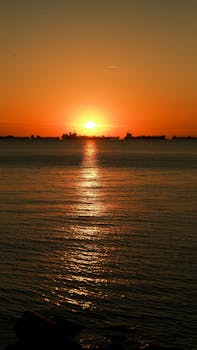 Breathtaking view of the sun setting over the ocean with silhouetted ships on the horizon.