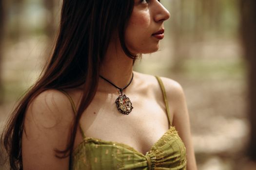 Close-up of a woman in a green dress with a floral pendant necklace in a serene forest setting.