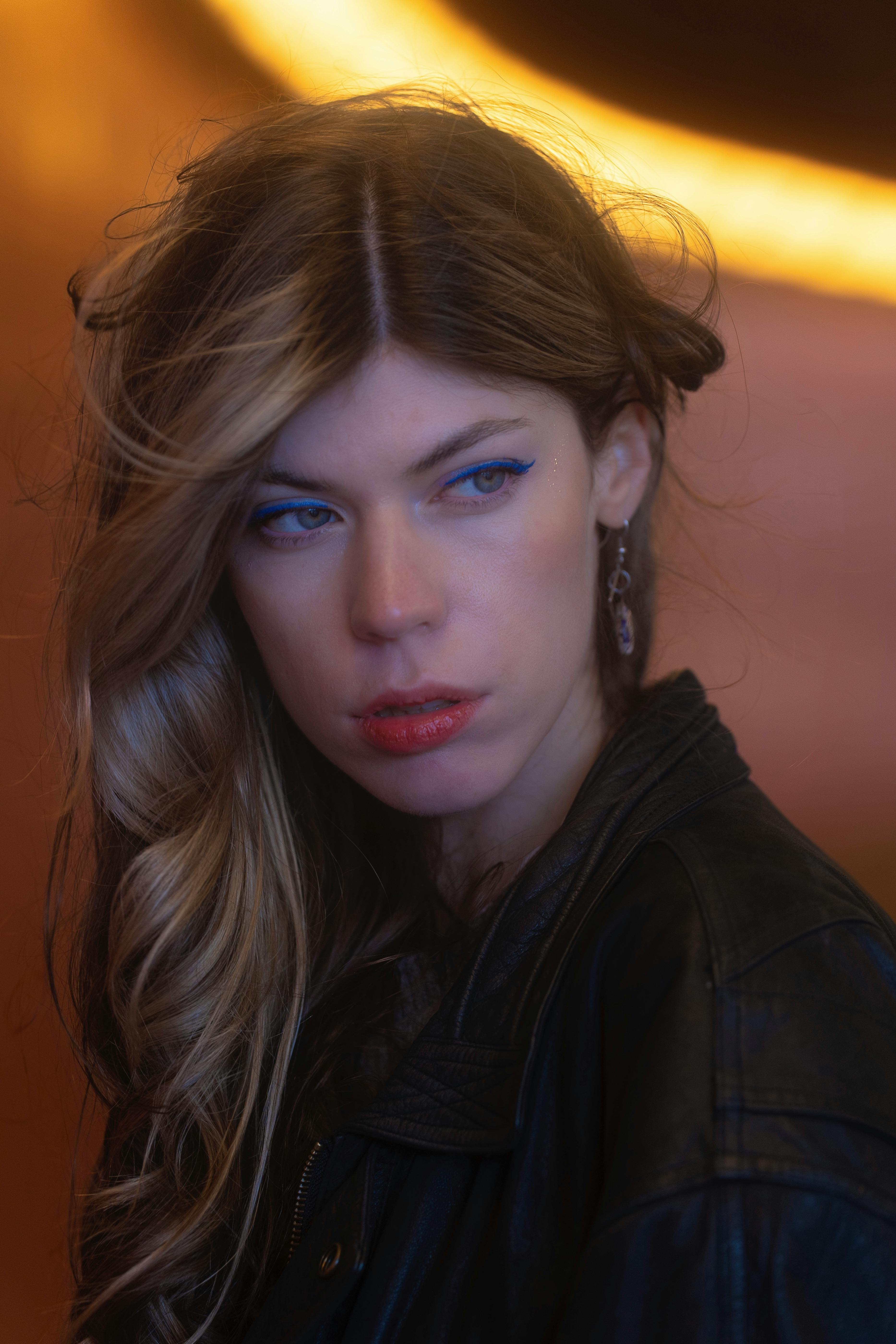Free Artistic portrait of a woman with bold blue eyeshadow and leather jacket in dim lighting. Stock Photo