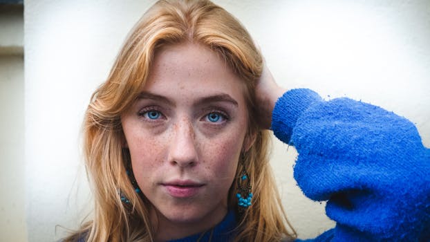 一张特写肖像，画中是一位金发蓝眼、面带雀斑、身着蓝色毛衣的女子