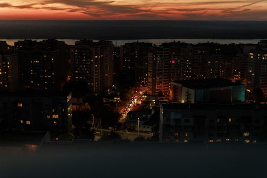 Elevated view of a city skyline during dusk with building lights glowing and a vivid sunset.