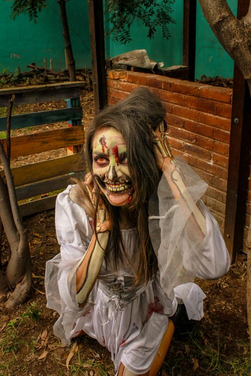 Free Woman with skull makeup kneels in a rustic setting, embodying spooky Halloween vibes. Stock Photo