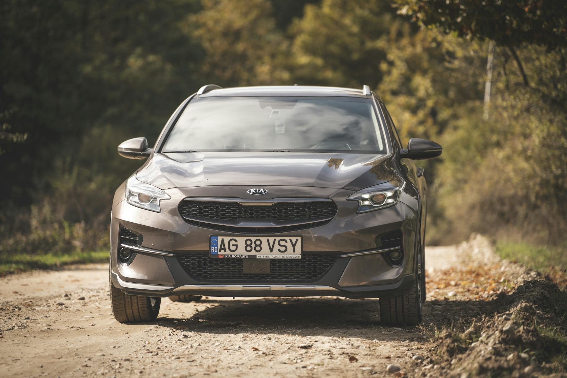 Front view of a Kia car on a dirt road, surrounded by autumn foliage in a rural area.