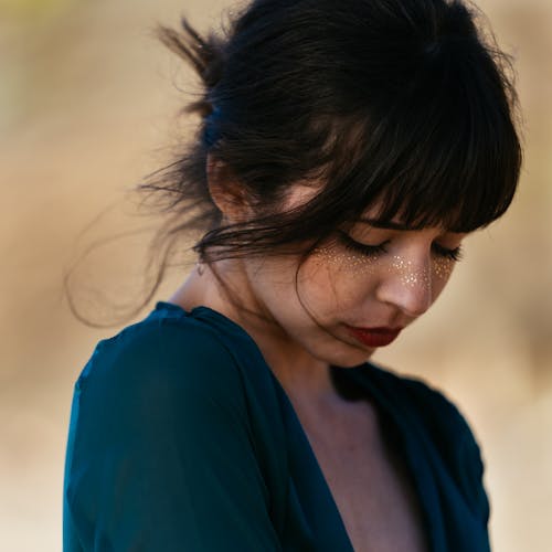 Portrait Photo of Woman Wearing Blue Top with Glitter on Her Face Looking Down