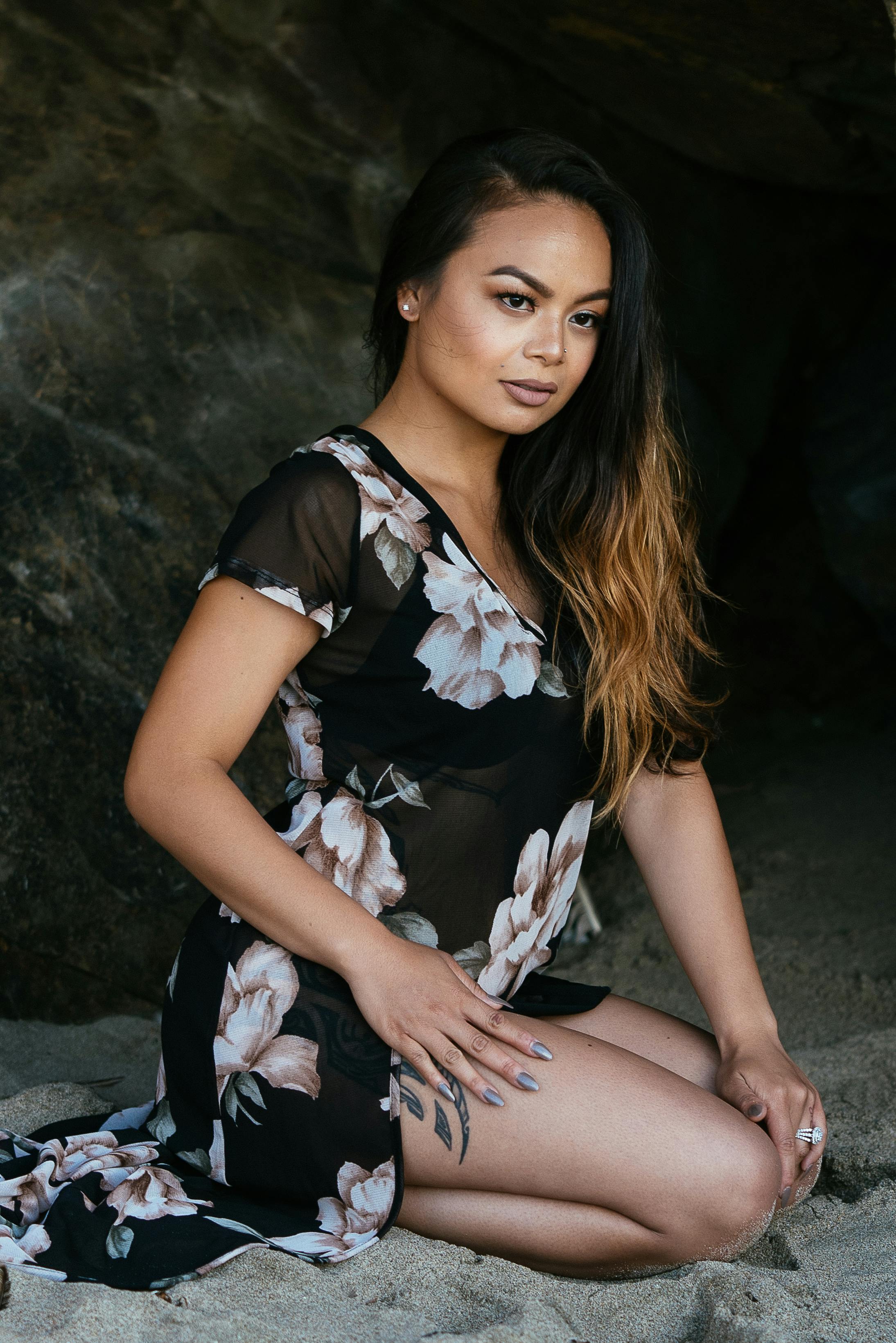 woman in black and white floral cap sleeved dress sitting down on sand