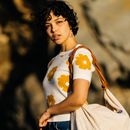 一位穿着花卉毛衣、背着大袋子的时尚女性在户外自然光线下摆姿势