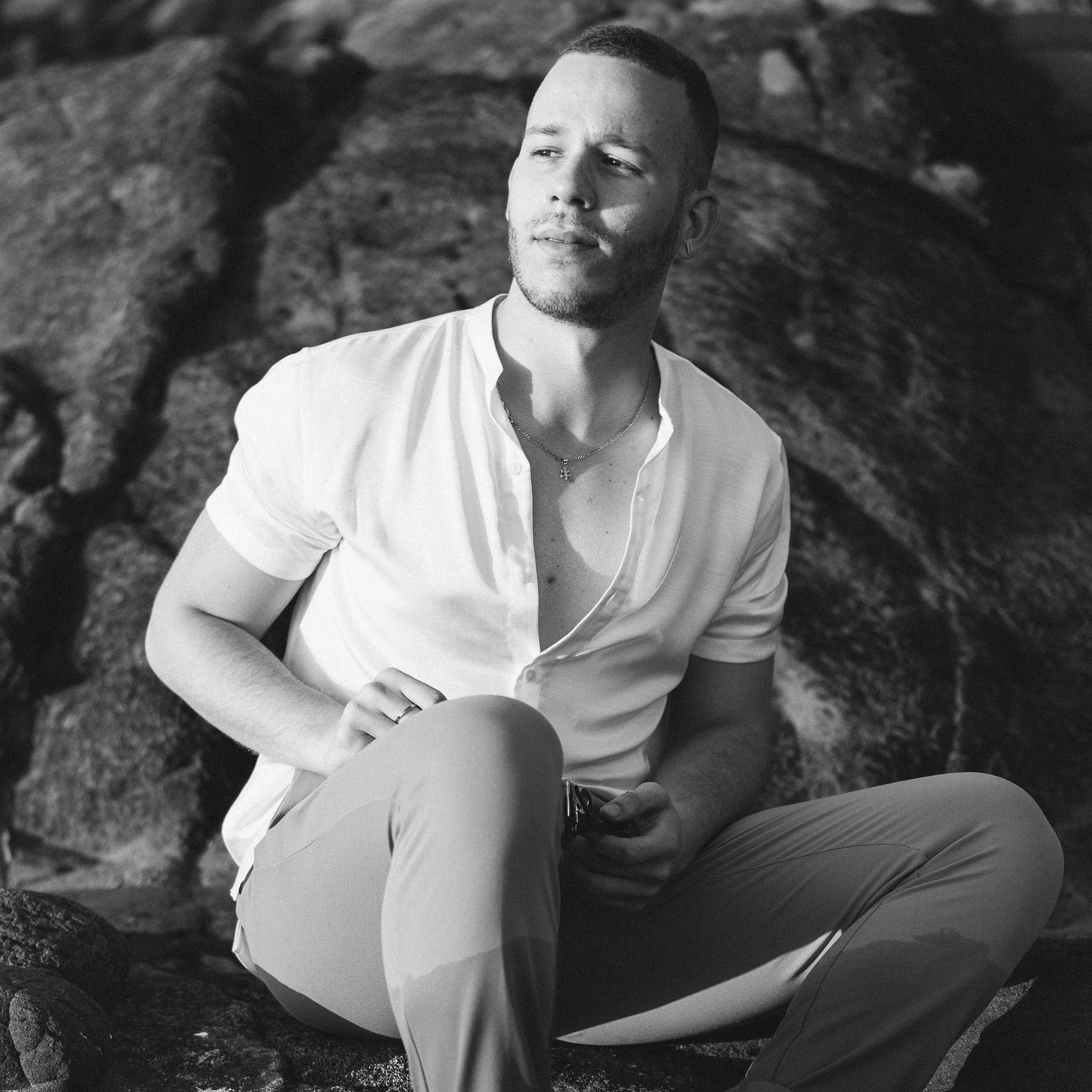 一名时尚男子在户外单色照片中，放松地坐在岩石上