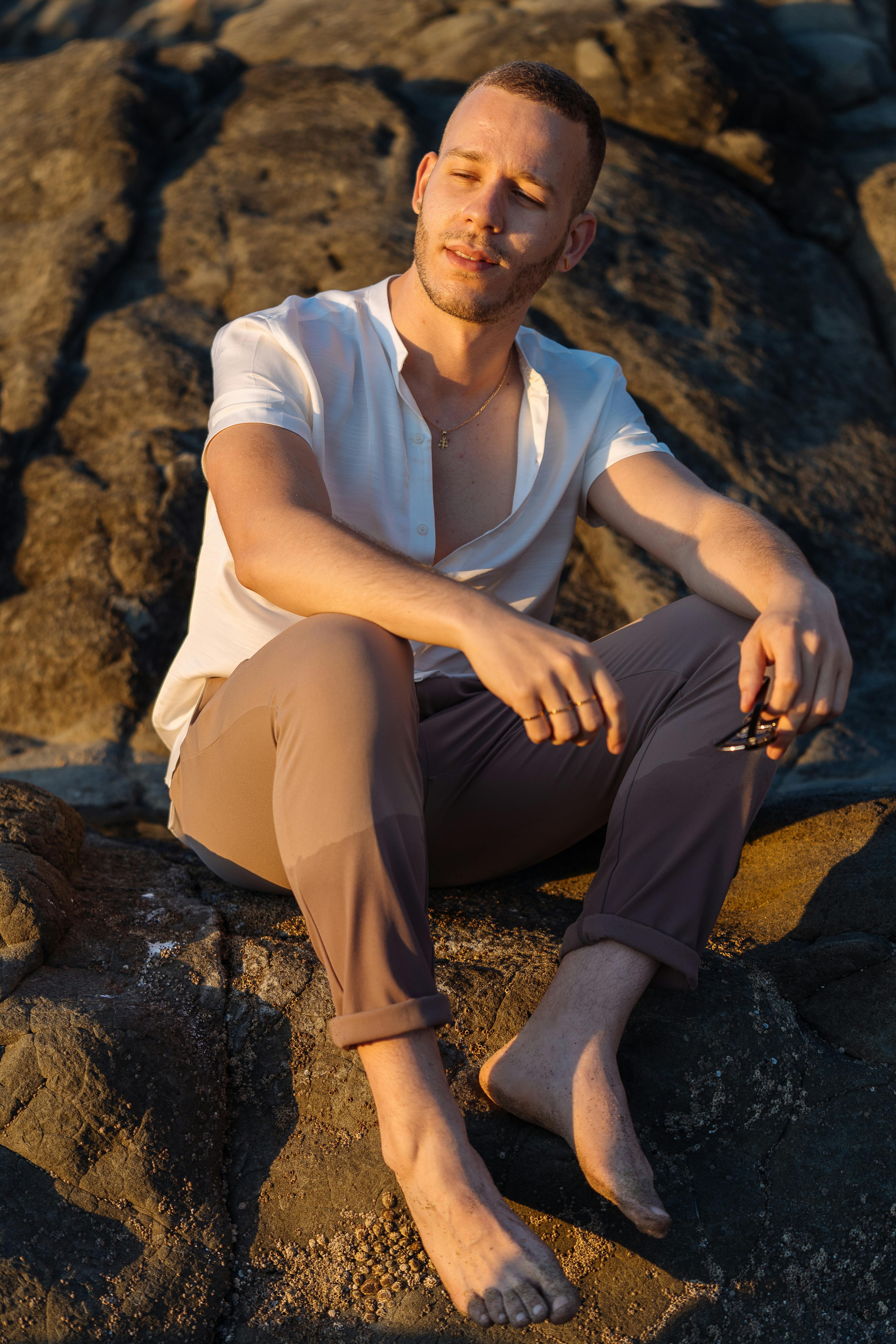 日落时分，一位身着休闲装的时尚男士坐在岩石上，气质轻松