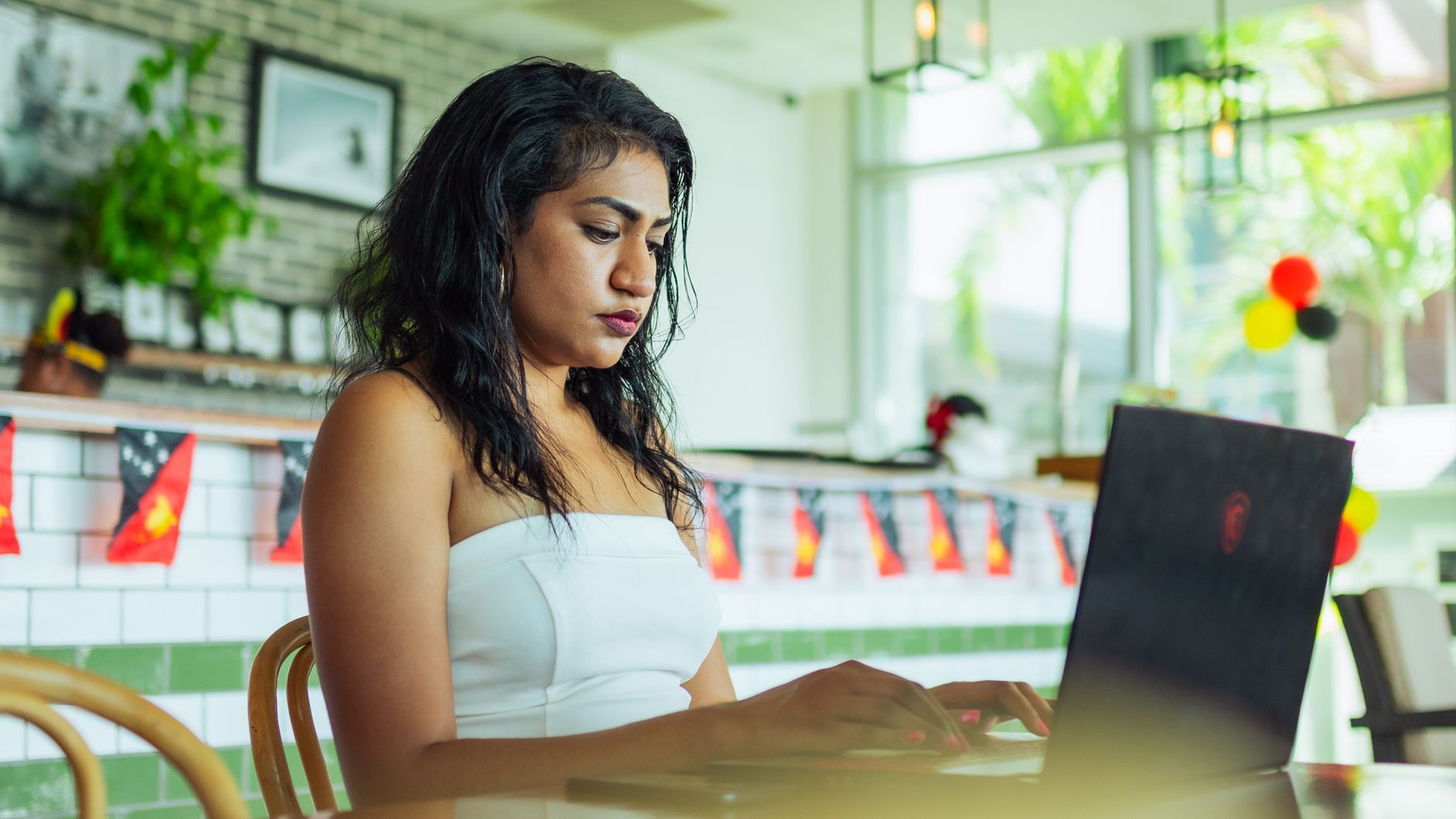 Focused woman working on a laptop in a bright indoor café environment.