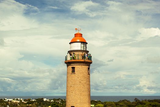 A scenic lighthouse with visitors atop, set against the vast Indian Ocean and blue sky.
