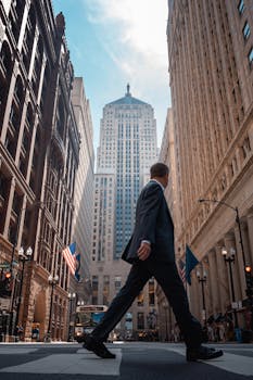 Businessman in suit crossing street in downtown Chicago with skyscrapers and flags.