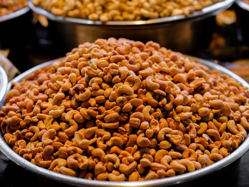 Free A close-up shot of freshly roasted cashews in a large metal bowl at a bustling market. Stock Photo