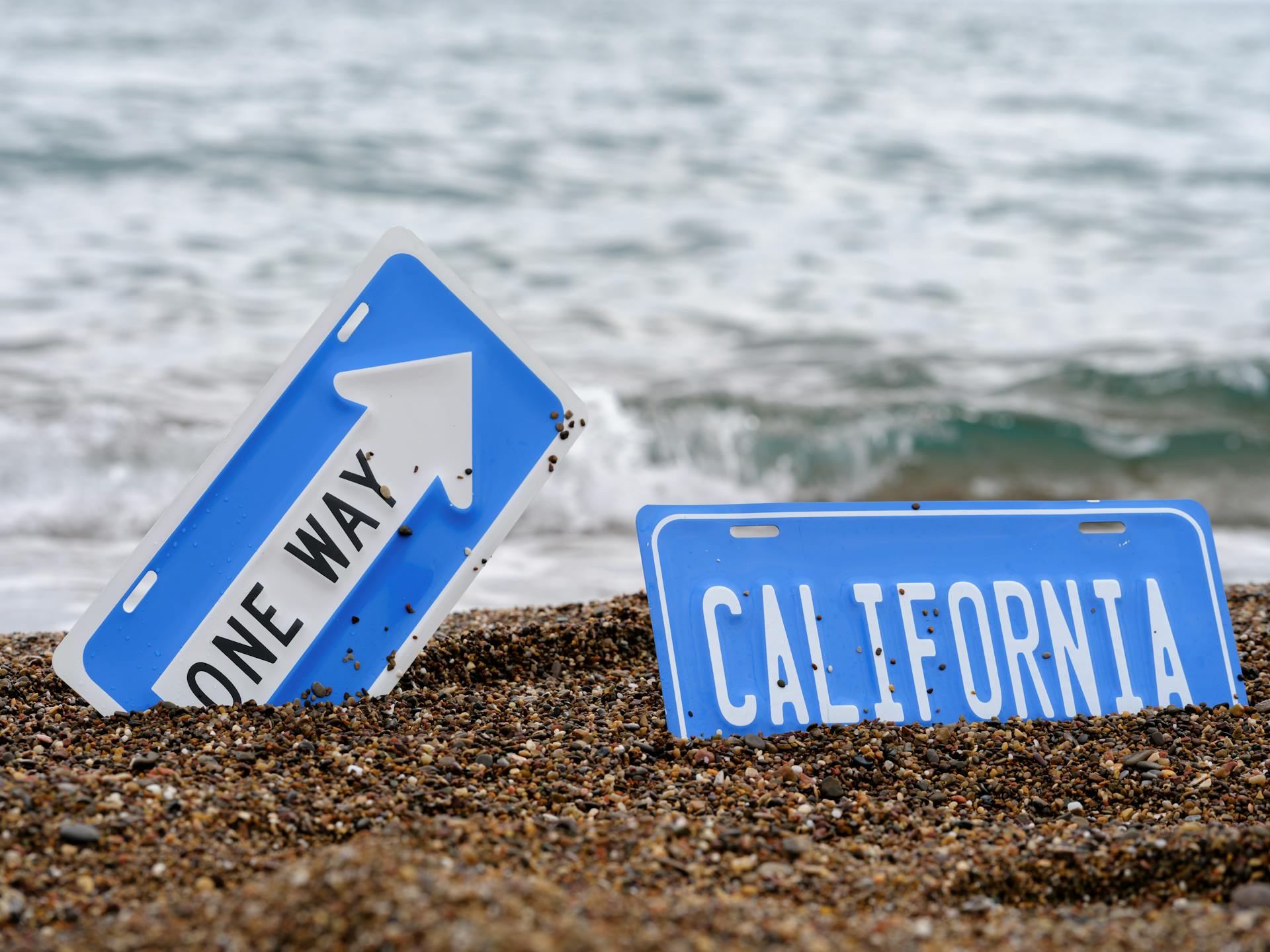 An artistic concept of California road signs partially buried in a beach with ocean waves.