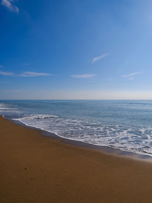 Free Relaxing beach scene with gentle waves and clear blue sky, ideal for travel and nature themes. Stock Photo