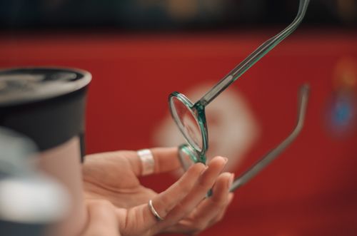 Free Stylish eyeglasses held by a hand against blurred red background, showcasing fashion and elegance. Stock Photo