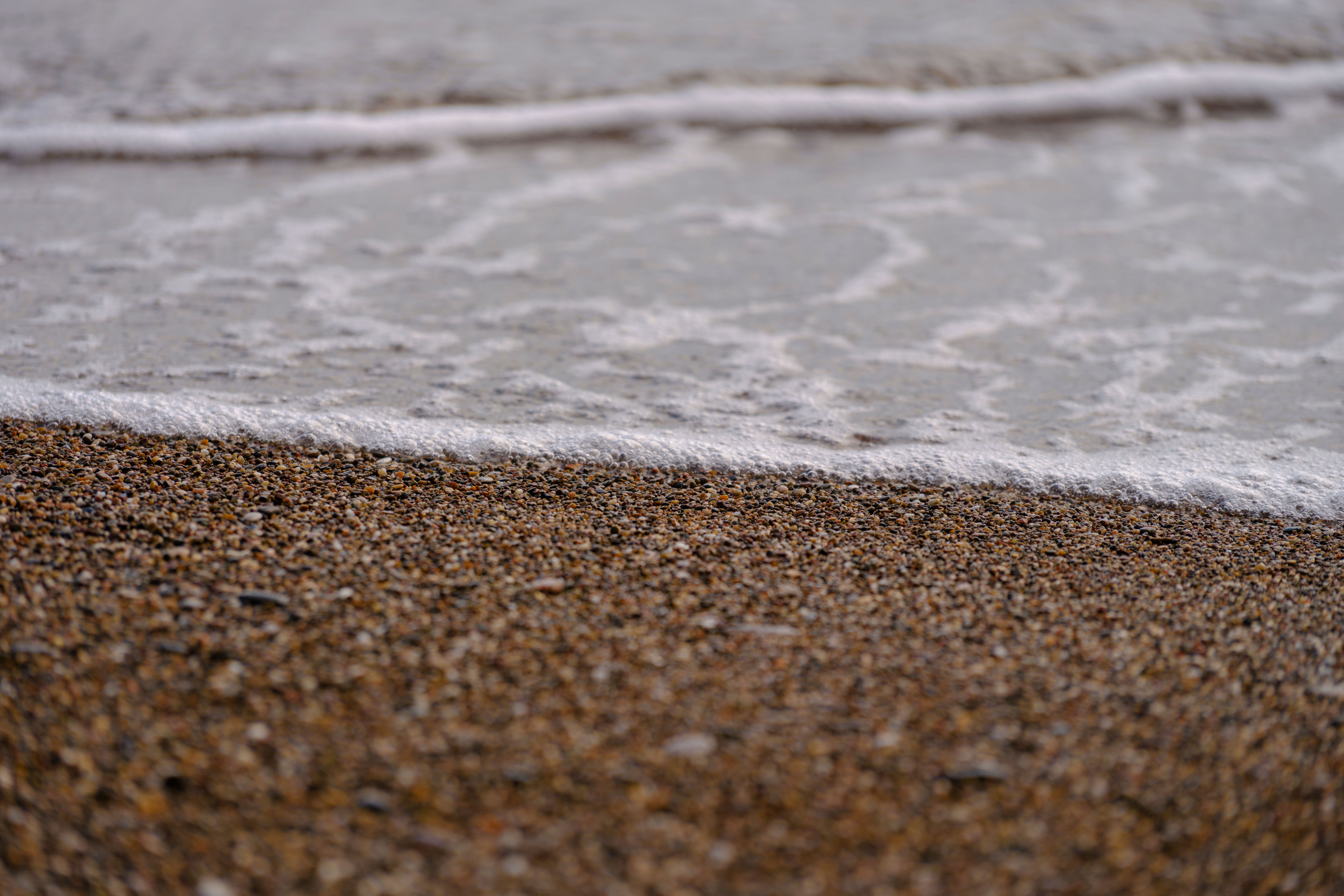 Close-up of a pebble beach with waves gently crashing, creating a textured landscape scene.