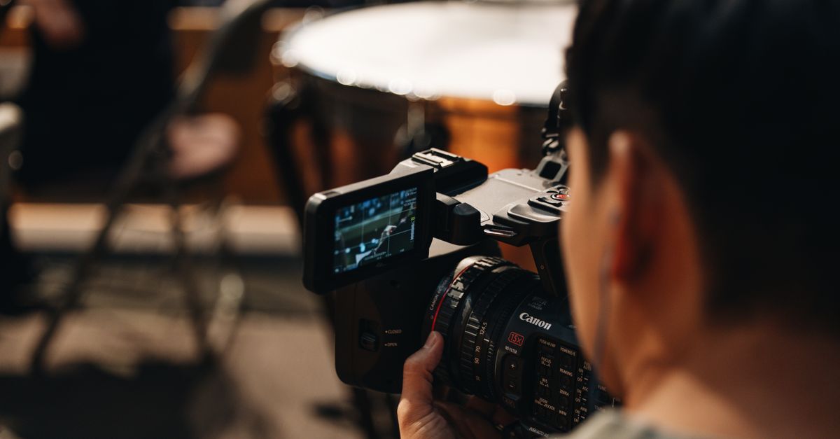 A close-up shot of a Ghanaian man smiling while operating a camera or editing equipment in a modest church setting