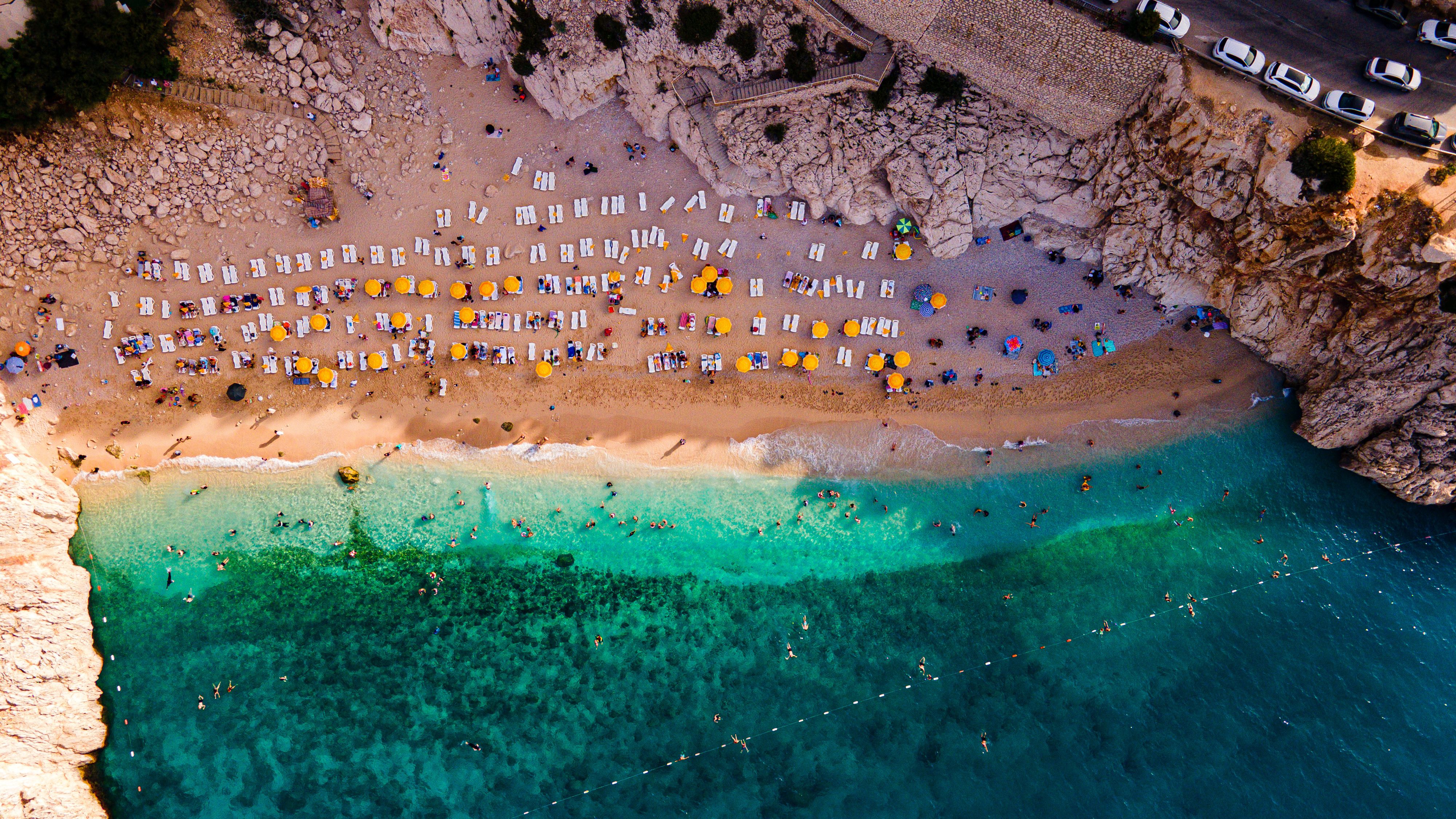 Aerial shot of a busy beach with umbrellas and turquoise sea, perfect for summer vibes.