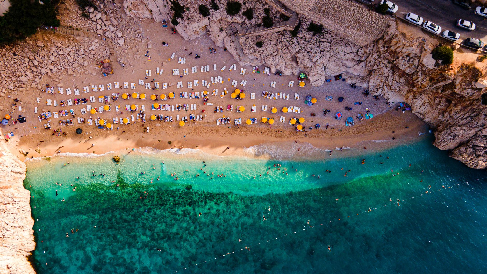 Aerial shot of a busy beach with umbrellas and turquoise sea, perfect for summer vibes.