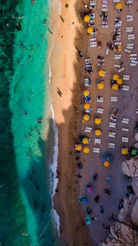 A stunning aerial view of a lively beach with vibrant turquoise waters and yellow beach umbrellas.