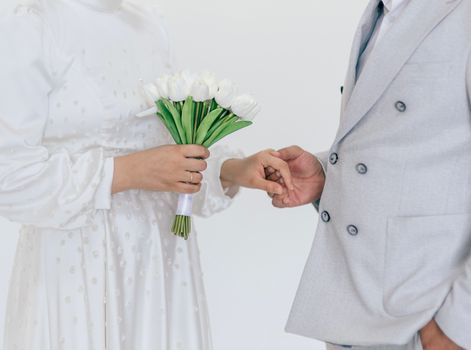 Elegant couple holding hands with white tulip bouquet, dressed in wedding attire.
