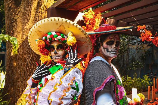 Two individuals in colorful Day of the Dead costumes pose outdoors. Festive and cultural.