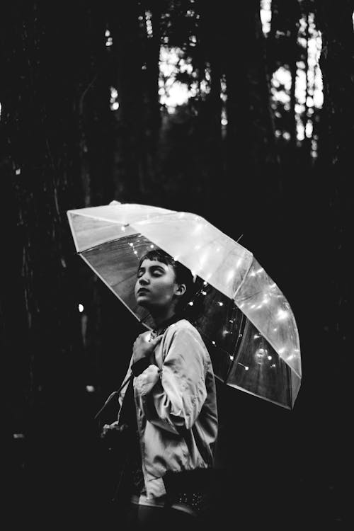 傘を持って雨の中を歩く女性のグレースケール画像