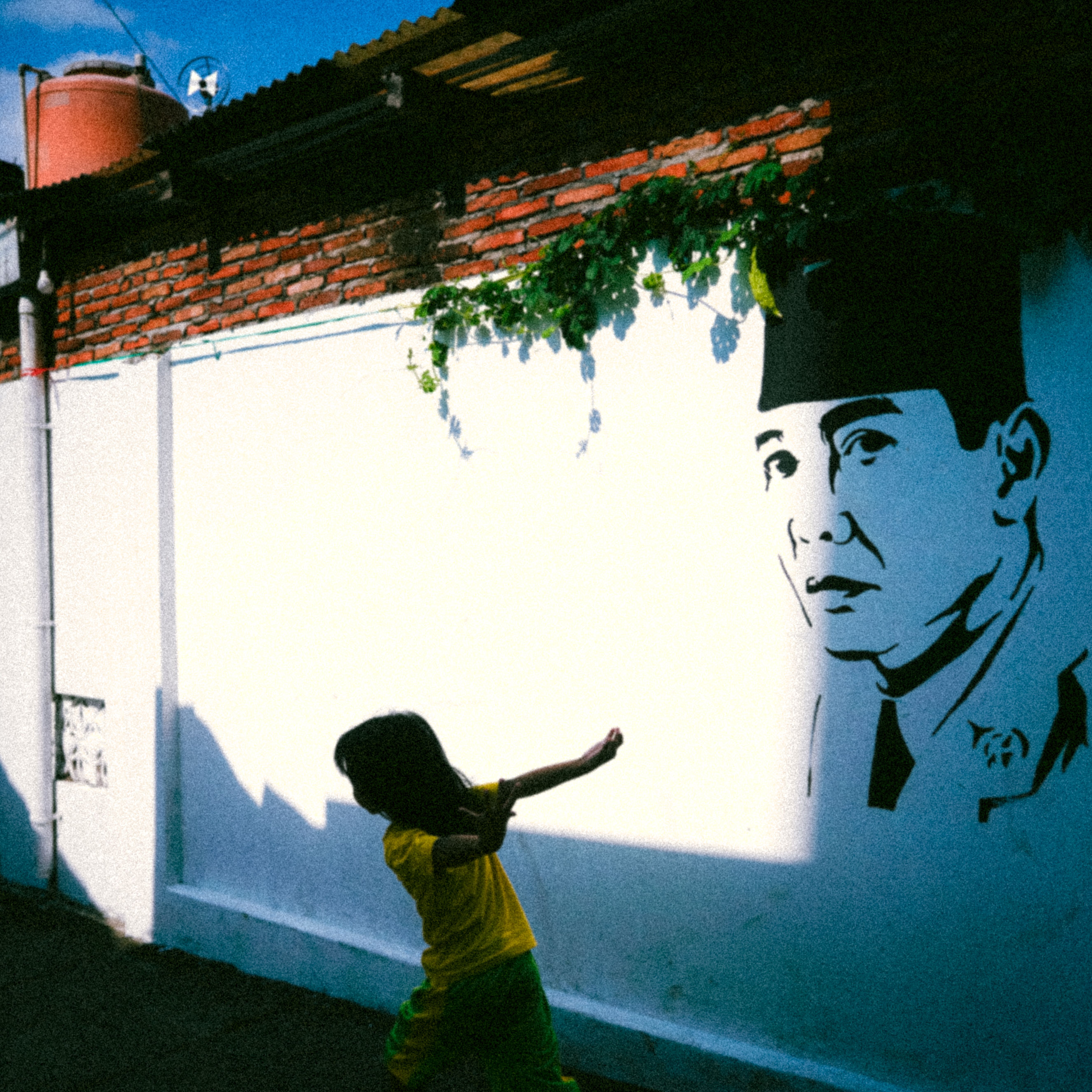 A child walks past a sunlit mural on a vibrant street, creating a dynamic urban scene.