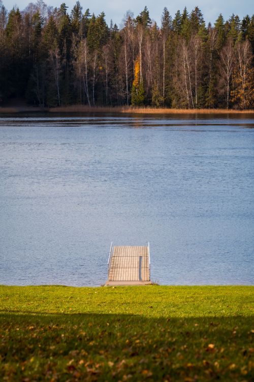 Free A tranquil lakeside view with a dock and vibrant autumn trees in the background. Stock Photo