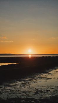 Beautiful sunset over calm coastal waters with a warm orange sky reflecting off the water surface.