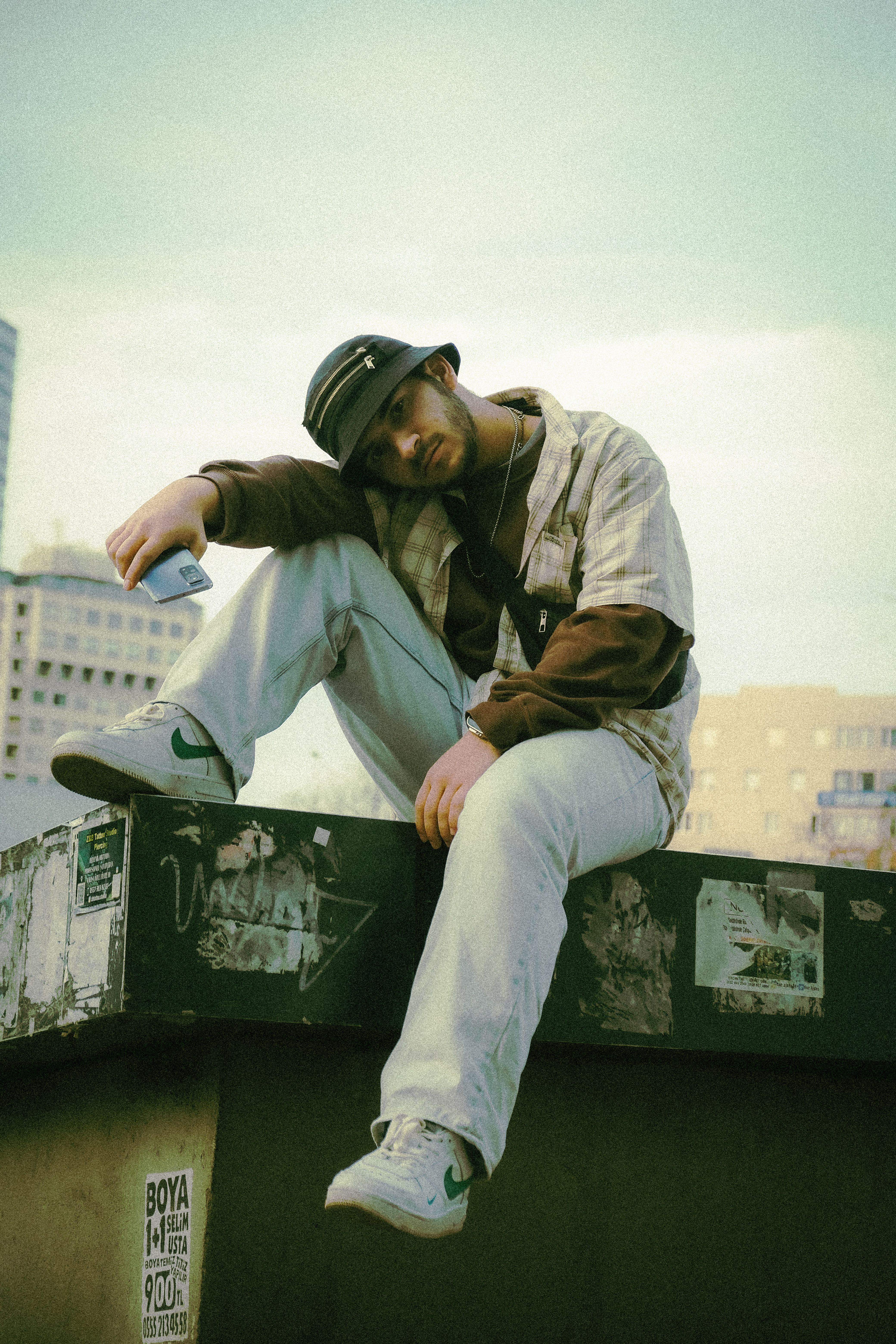 Young man in casual attire sitting on urban rooftop, exuding a cool and relaxed vibe.