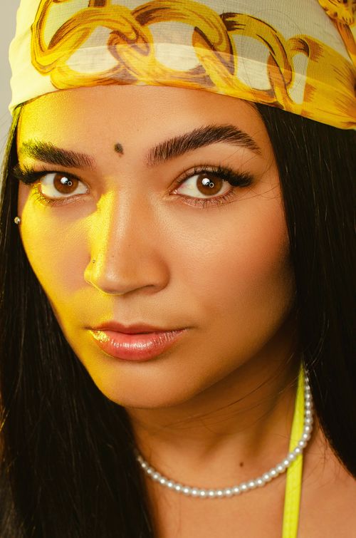 Free Close-up portrait of a woman wearing a vibrant yellow headscarf and pearl necklace. Stock Photo