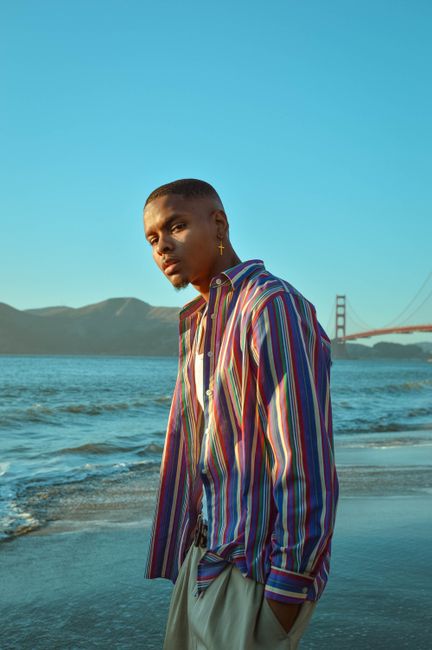 Fashionable man standing by the sea at sunset with Golden Gate Bridge.