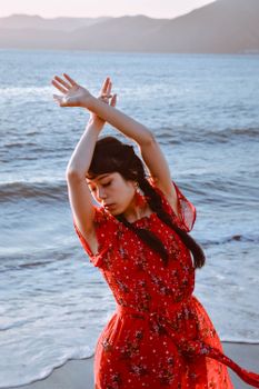 日落时分，一位身穿红色连衣裙的女子在海边优雅地摆着姿势