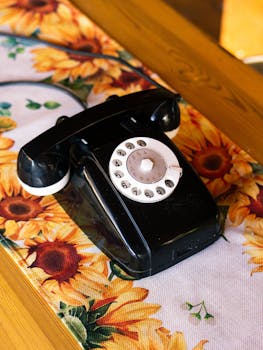 A vintage black rotary phone on a vibrant sunflower-patterned tablecloth, evoking nostalgia.