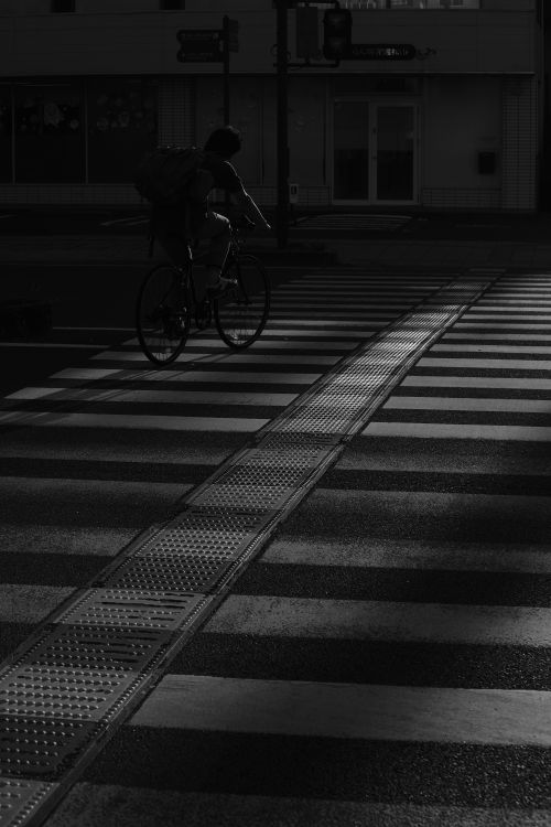 Free Dramatic black and white photo of a cyclist crossing an urban street at twilight. Stock Photo