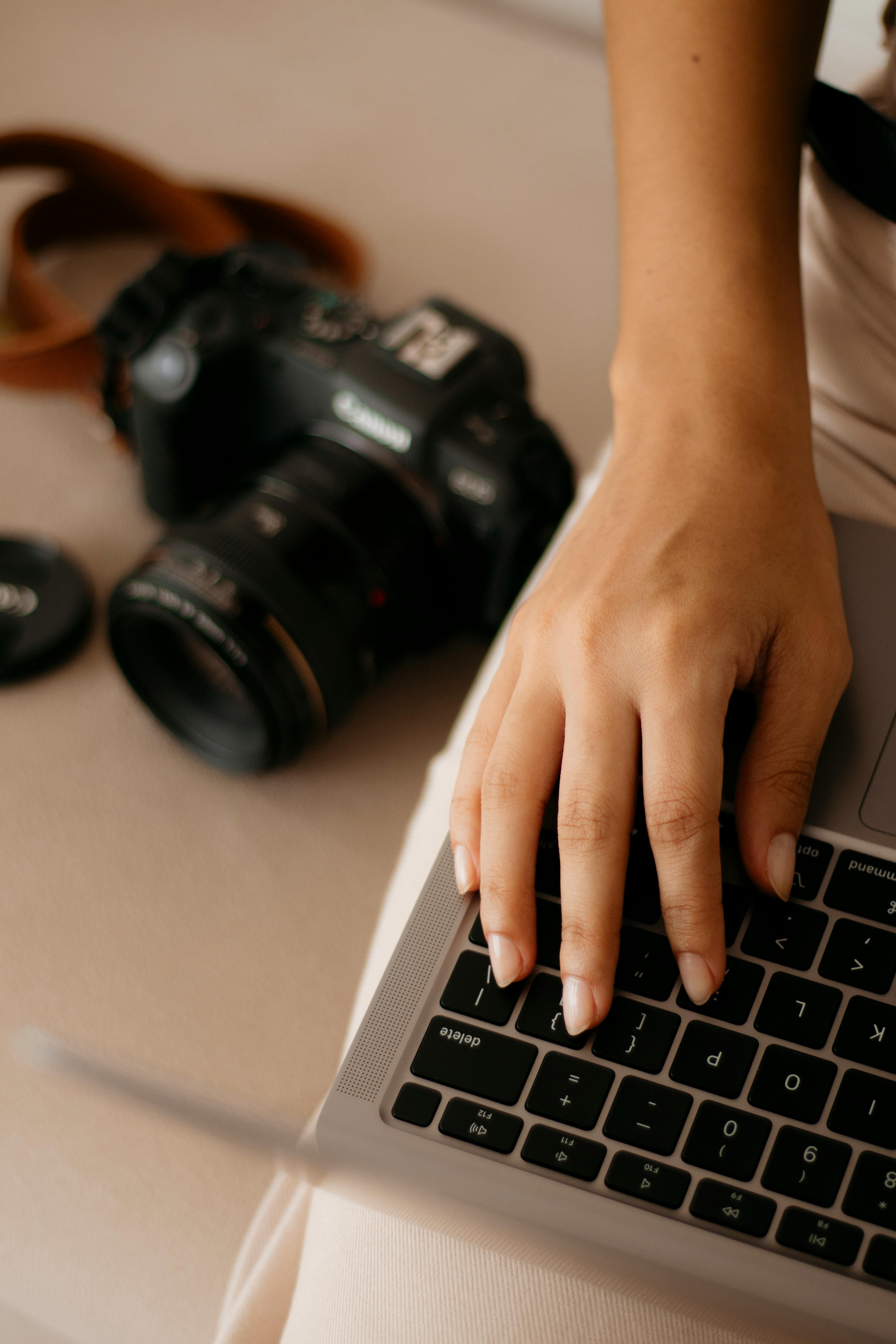 Close-up of a hand using a laptop beside a DSLR camera, perfect for tech or photography themes.