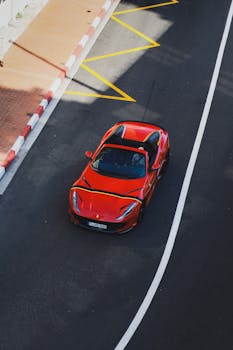 Aerial view of a red sports car driving on a clean city street.