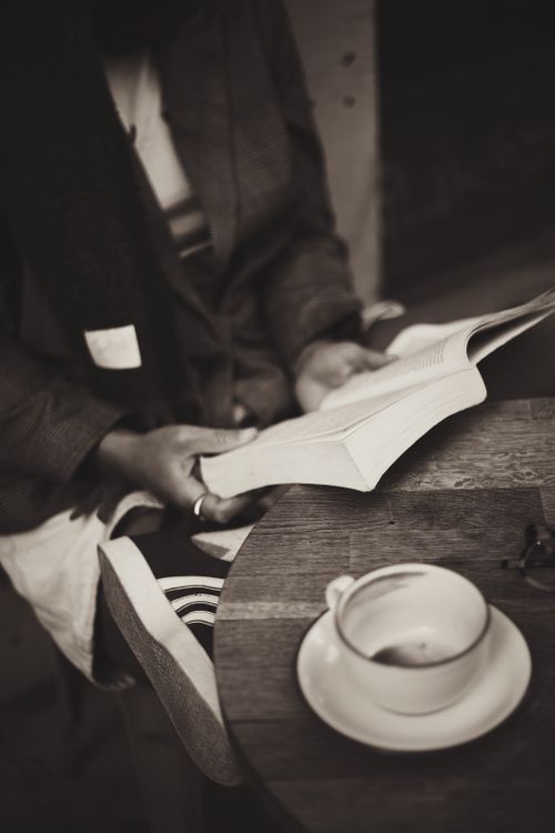 Free A tranquil scene of a person reading a book alongside a cup of coffee in a cozy cafe. Stock Photo