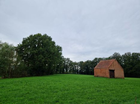 Peaceful countryside scene featuring lush green field and rustic brick barn under cloudy sky.