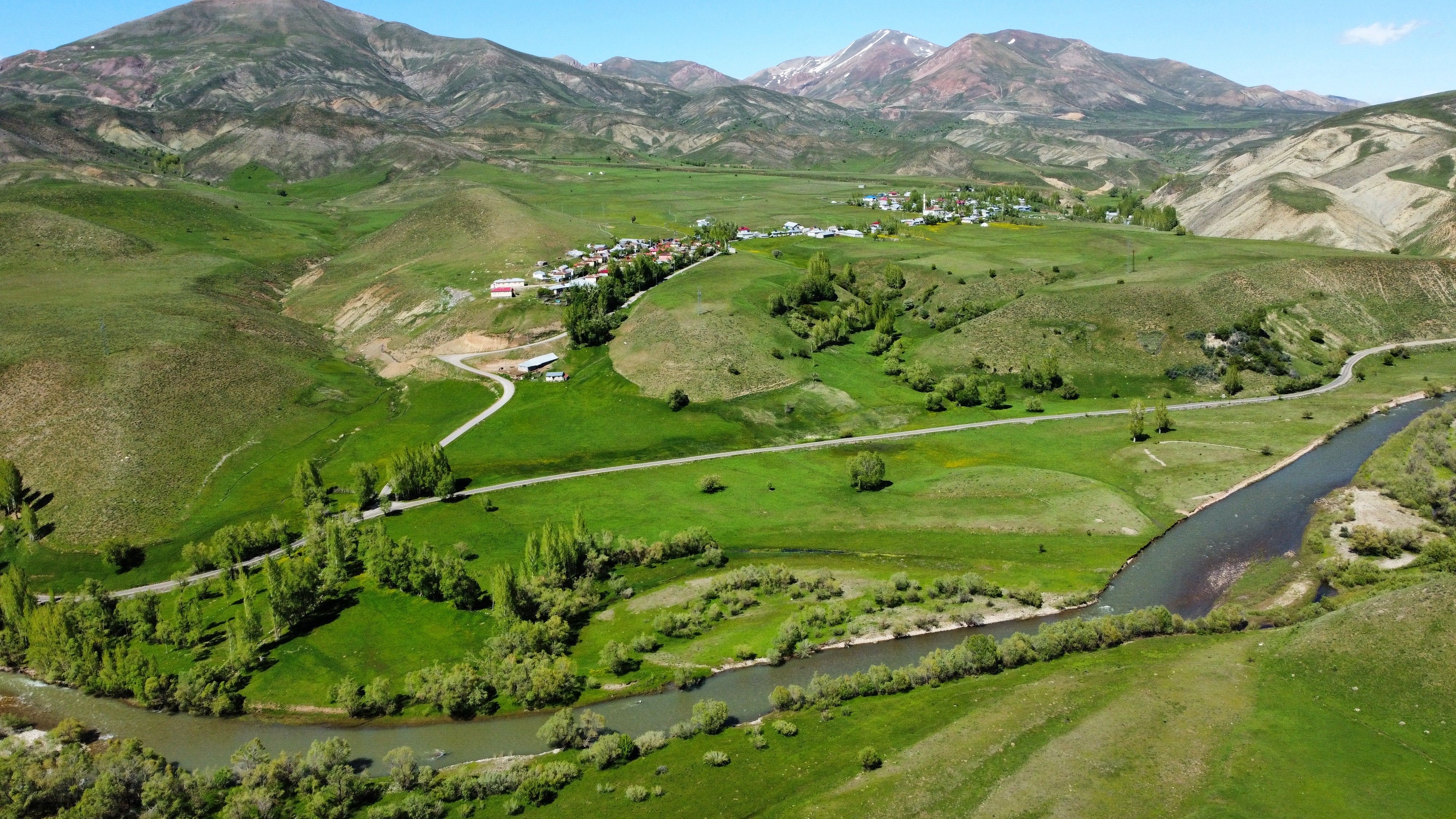Aerial view of a tranquil rural village surrounded by lush green hills and a winding river.