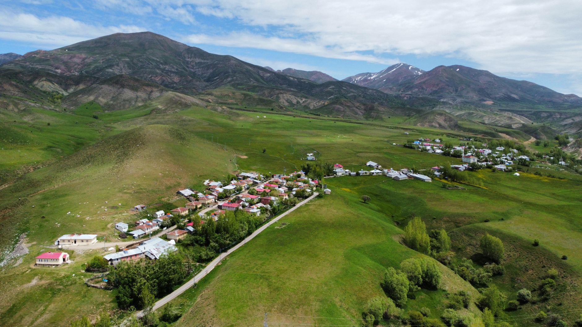 A stunning aerial view of a remote village nestled in lush green hillsides, under a bright sky.