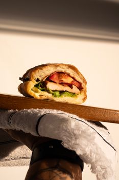 Close-up of a gourmet sandwich with fresh ingredients on a wooden board, side-lit for a dramatic effect.