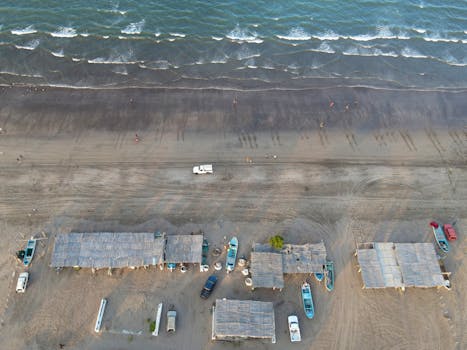 Aerial view of a coastal fishing village in Muscat, Oman showcasing fishing boats and beach huts along the sandy shore.
