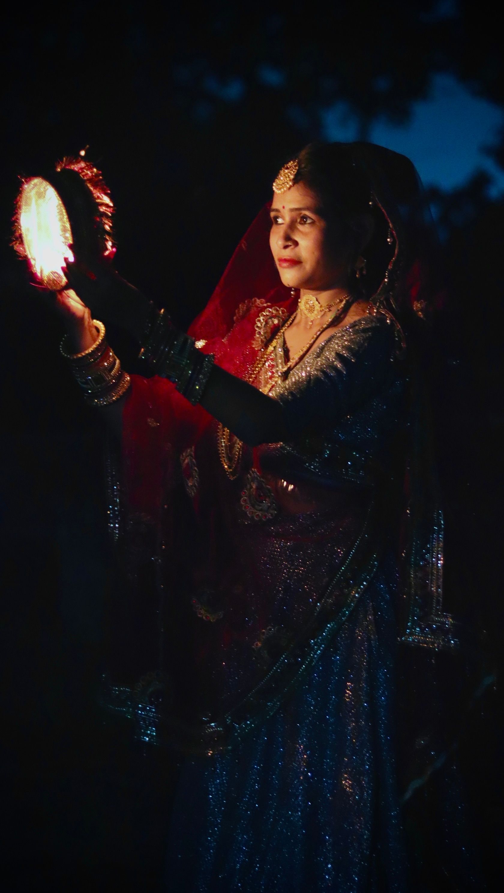 Woman wearing traditional Indian attire holding a decorative lamp during nighttime.