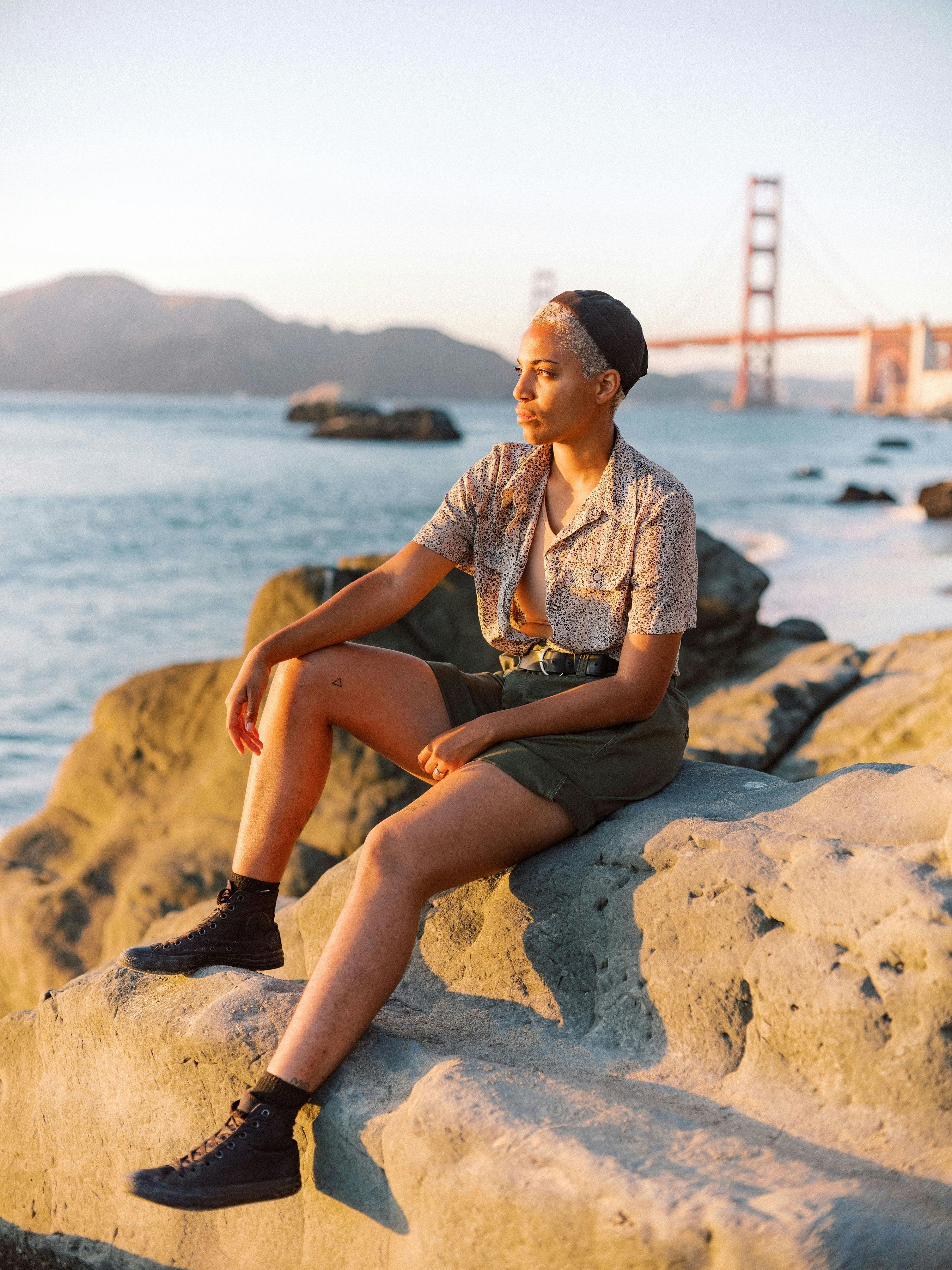 日落时分，一名穿着休闲装的女子坐在金门大桥附近的岩石上