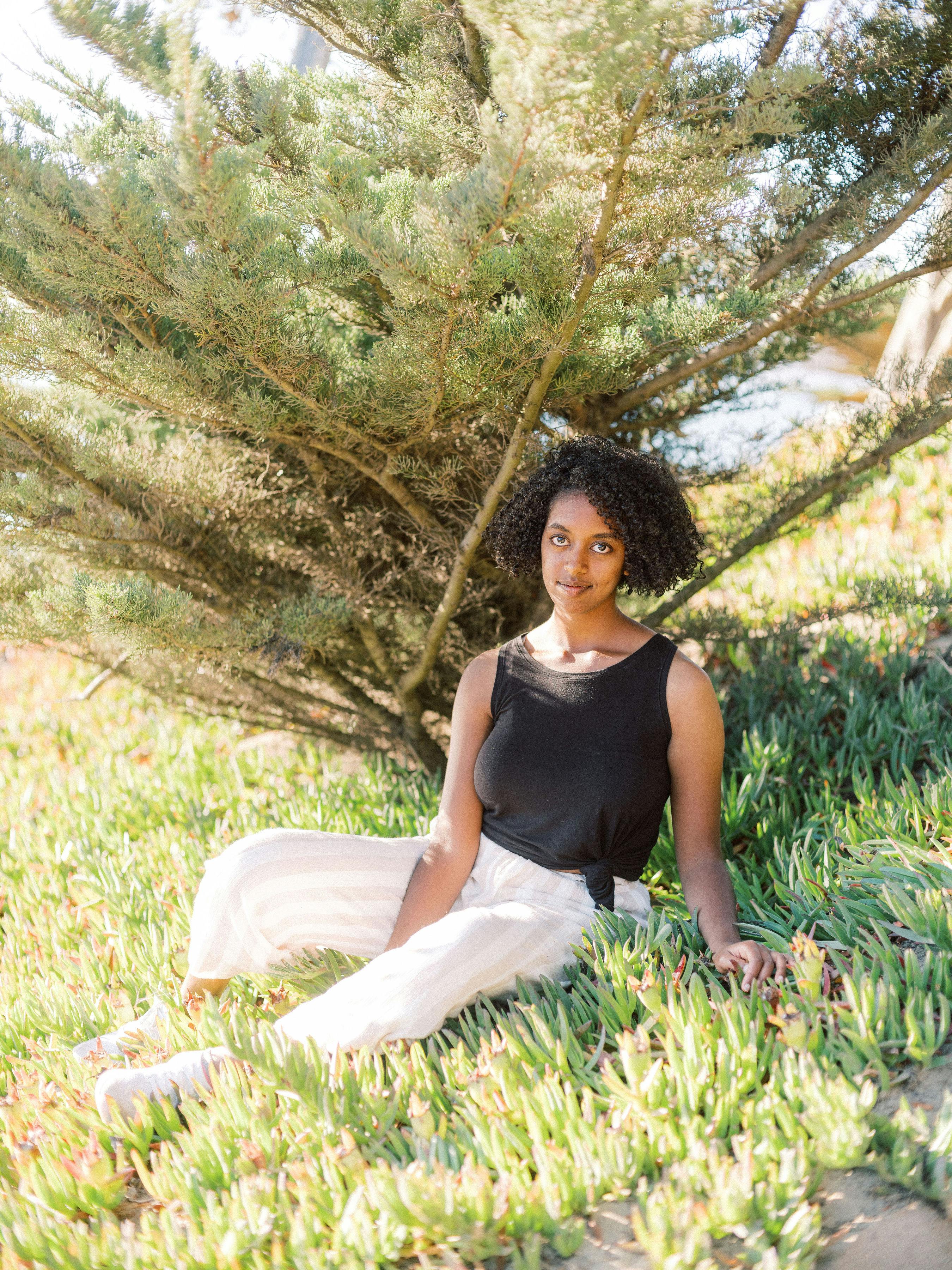 一名妇女坐在阳光明媚的花园草地上，在树下享受着宁静的时刻